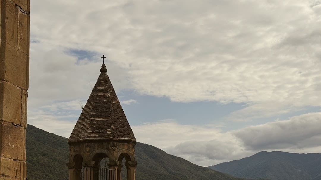 Stone tower with cross against cloudy sky and mountains
